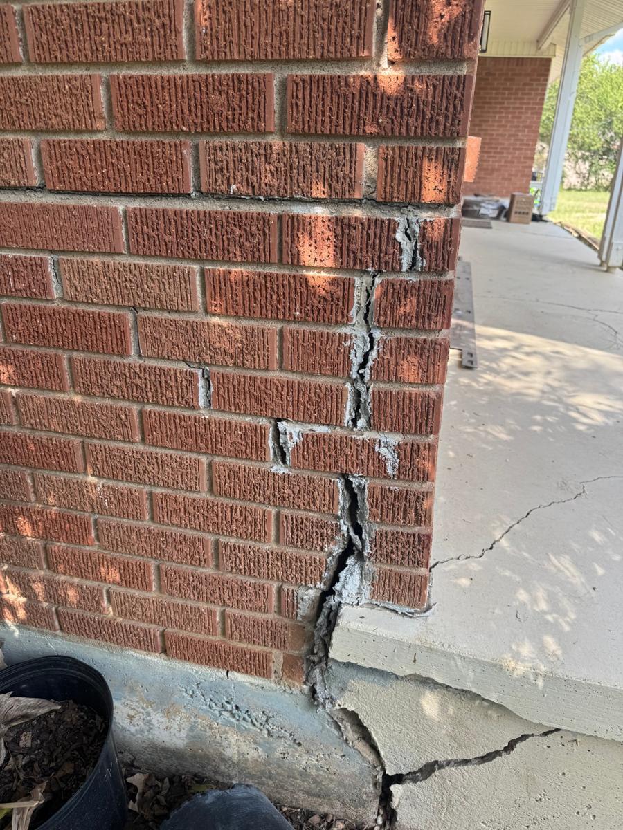 Brick wall split open in a stair-step crack where it meets a cracked porch slab