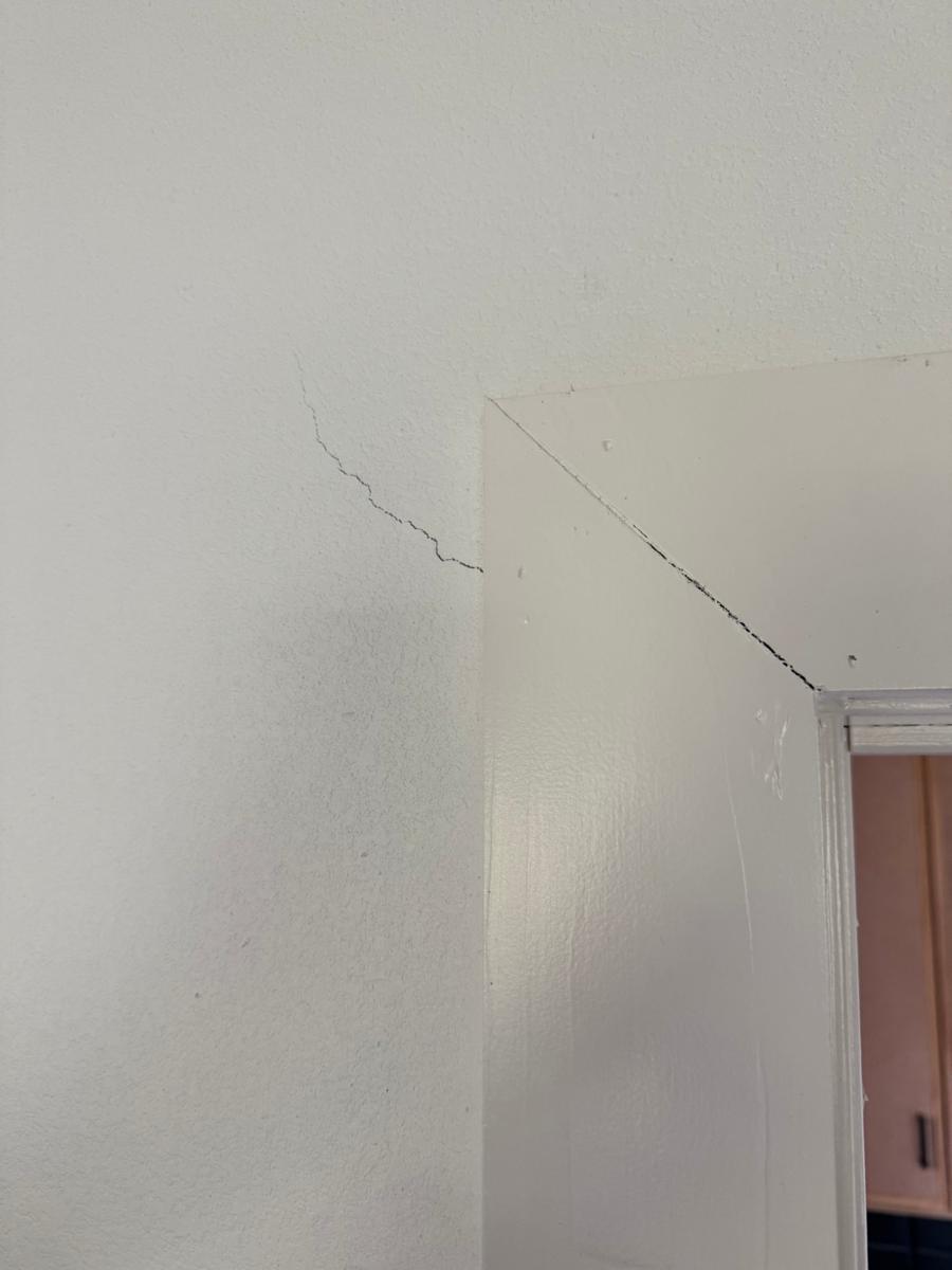 Drywall crack running from the corner of a door frame, with the trim joint opening